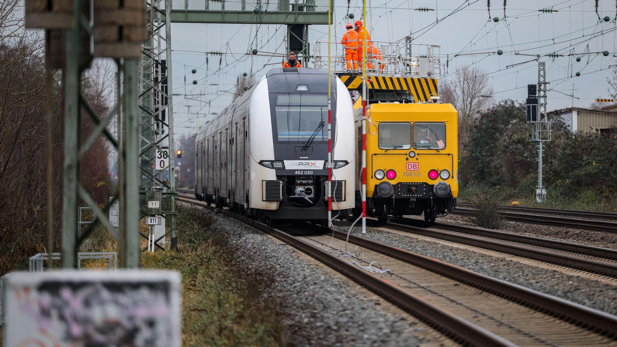 Ein Zug steht auf offener Strecke auf den Gleisen, rechts daneben ein Reparaturzug mit Monteuren, um den Oberleitungsschaden zu beheben.