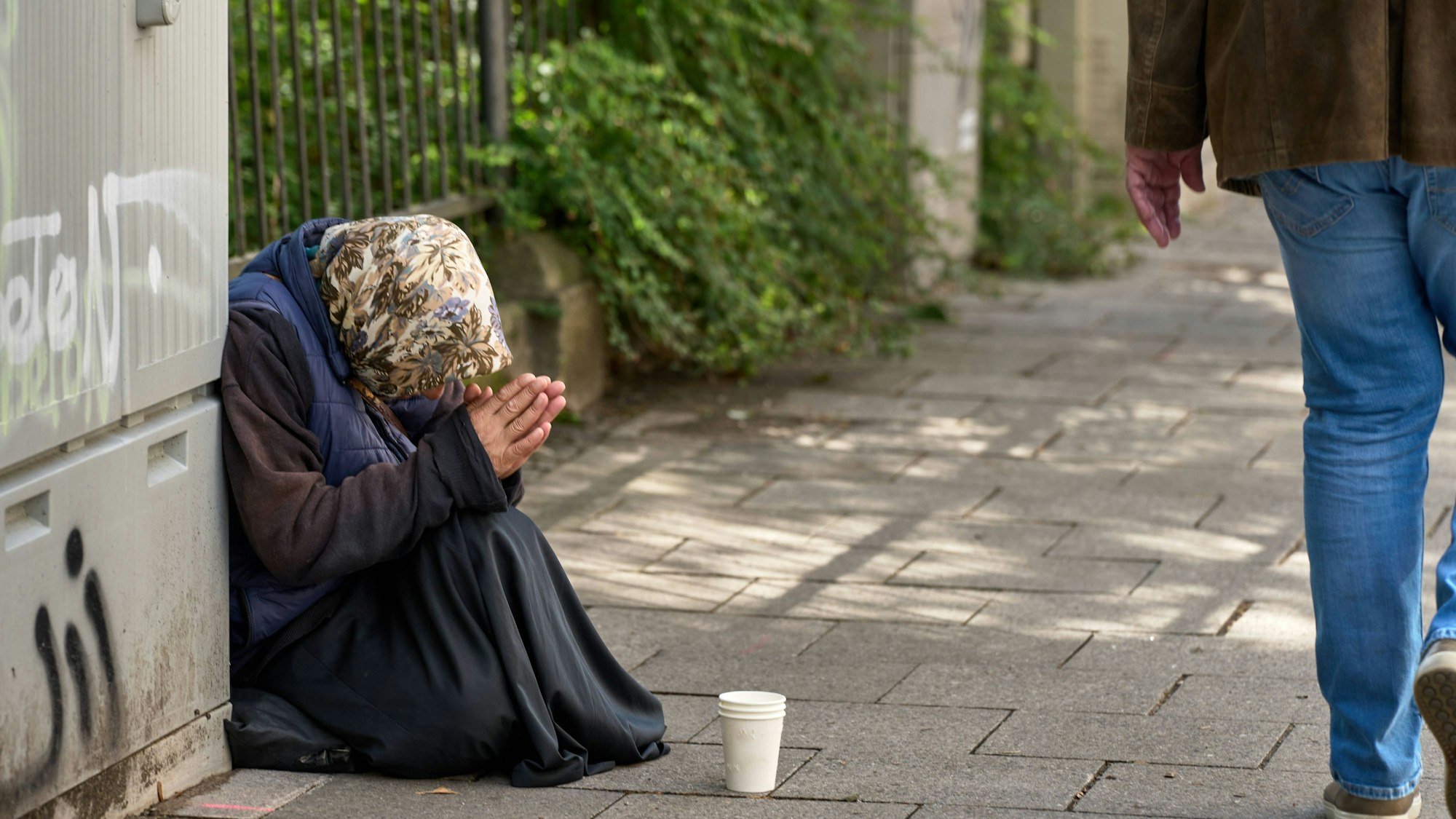 Ältere Frau bettelt auf Bürgersteig, Passant geht vorbei