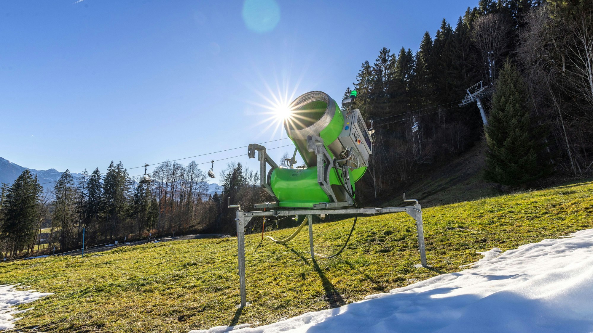 Schneekanone auf grüner Wiese mit teilweisem Schnee und Sonne