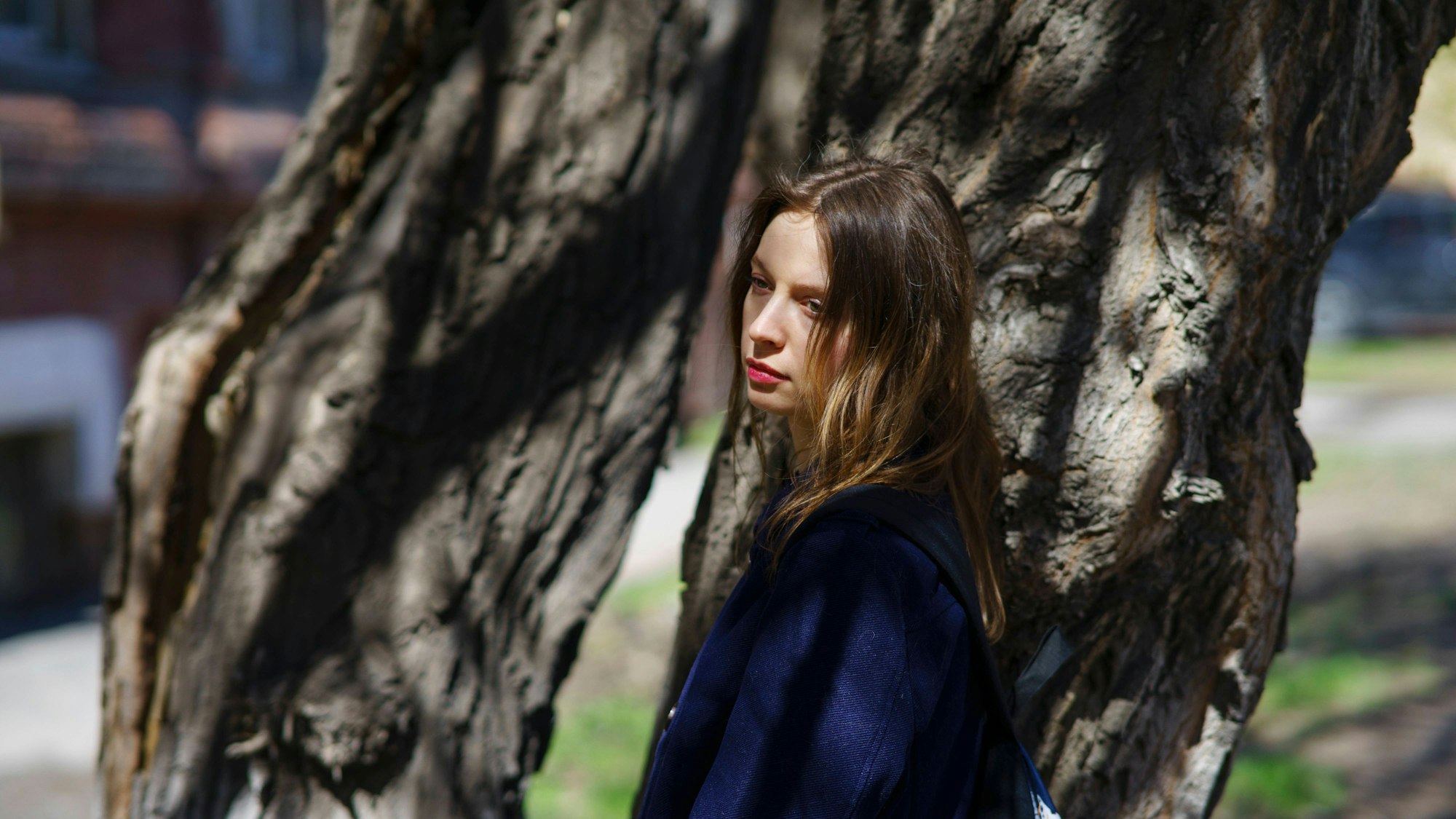 Junge Frau lehnt an Baum an sonnigem Tag