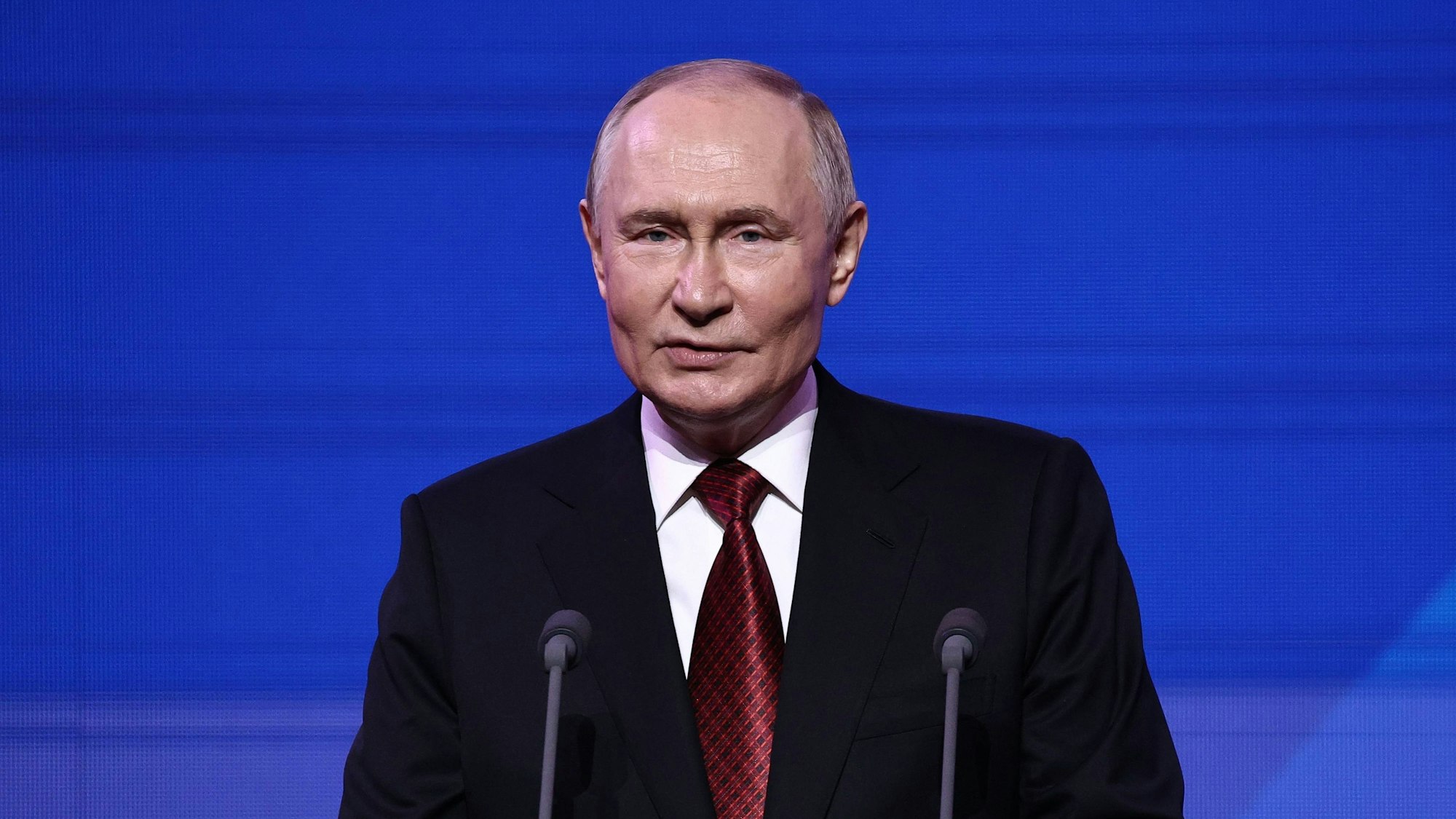 Wladimir Putin hält eine Rede vor blauem Hintergrund