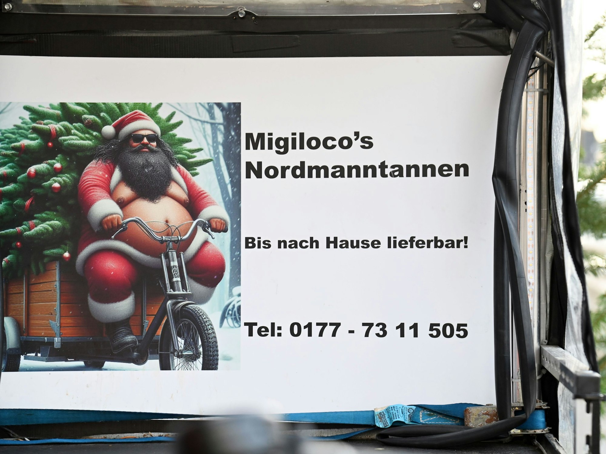 Auf einem Schild steht Migiloco's Nordmanntannen, bis nach Hause lieferbar, dazu eine Telefonnummer.