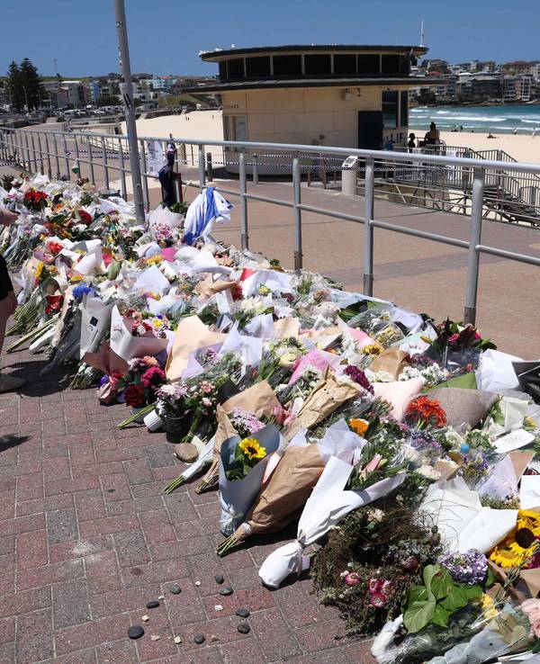 An der Strandpromenade liegen unzählige Blumensträuße in mehreren Reihen, auch zwei Frauen legen Blumen nieder.