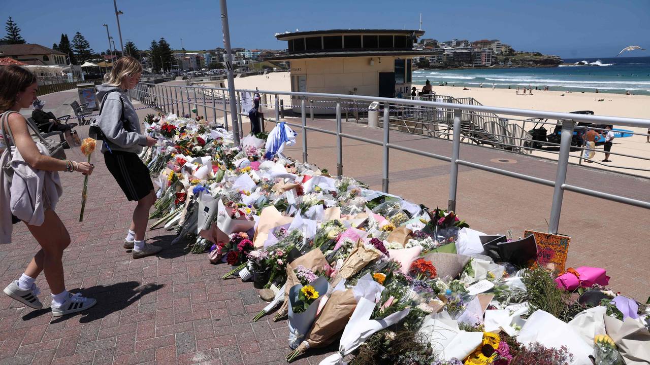 An der Strandpromenade liegen unzählige Blumensträuße in mehreren Reihen, auch zwei Frauen legen Blumen nieder.