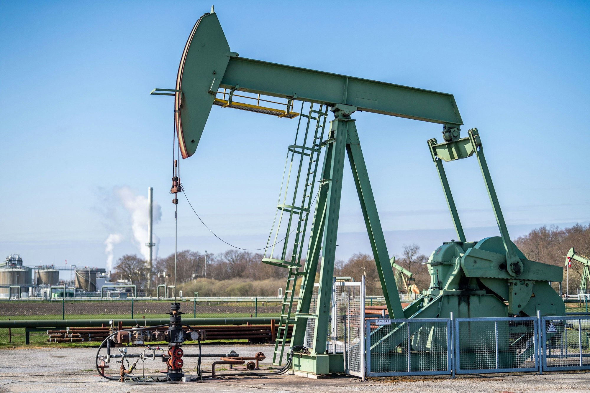 Eine Tiefpumpe für die Erdölförderung steht vor einer Raffinerie.
