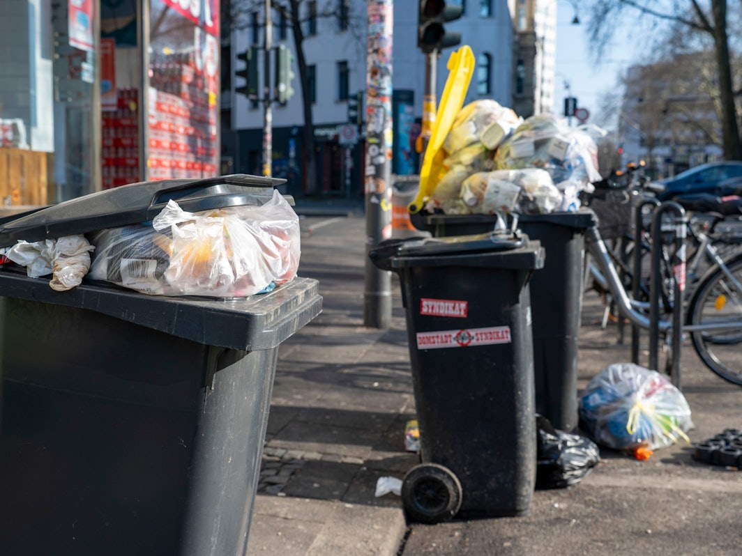 Mülltonnen stehen an einer Straße, zwei sind so voll, dass der Deckel nicht zu geht.