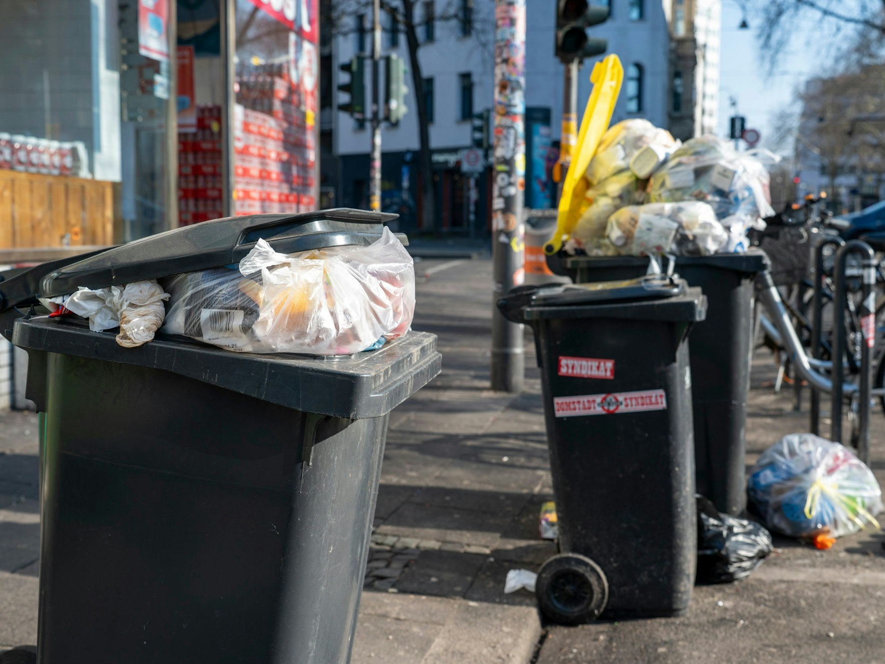 Mülltonnen stehen an einer Straße, zwei sind so voll, dass der Deckel nicht zu geht.