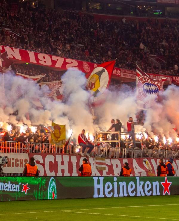 Die Fans des FC Bayern München zünden Pyro-Fackeln auf der Tribüne.