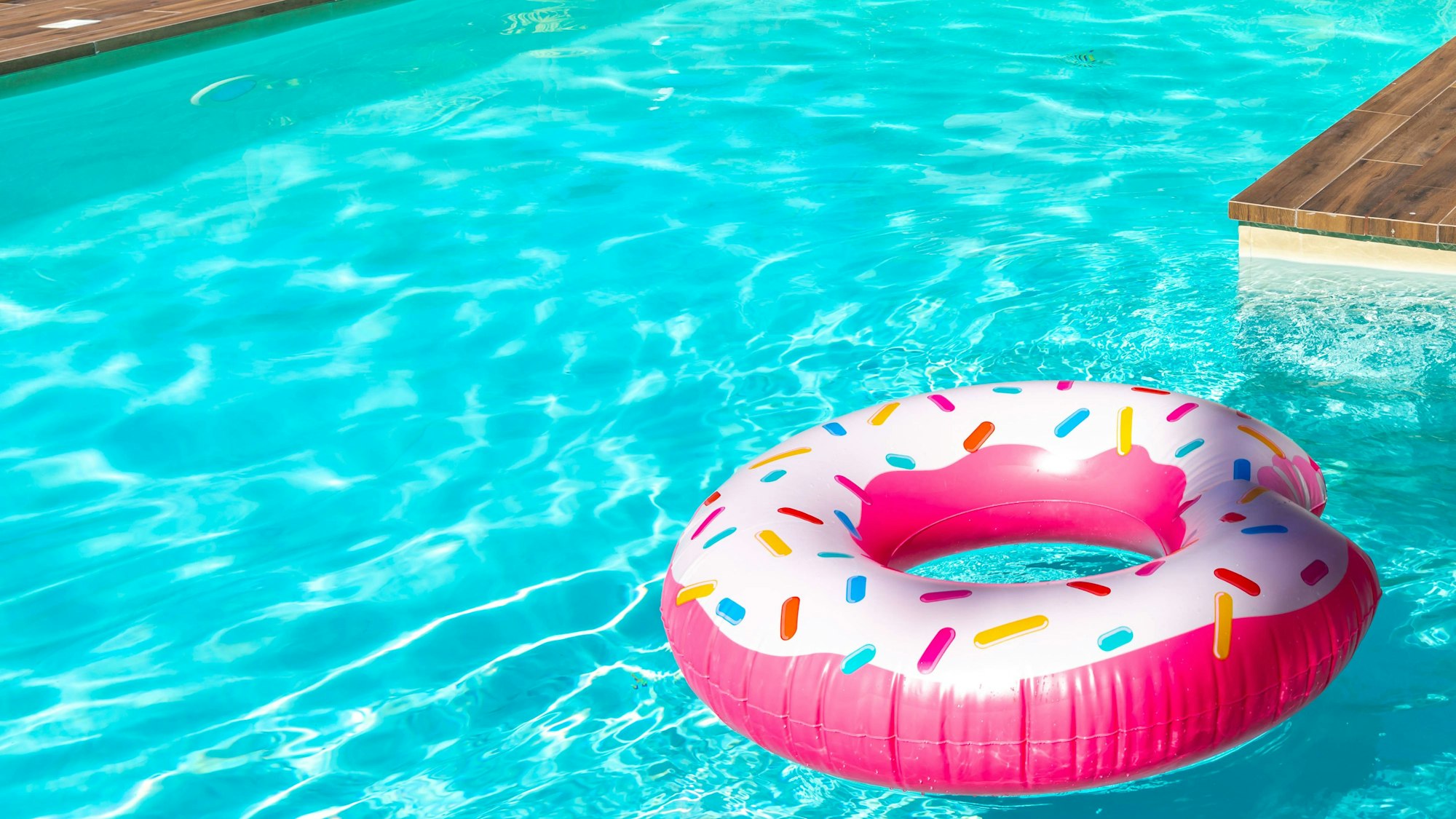 Rosa Donut-Schwimmring im türkisfarbenen Pool, von Maria Kraynova