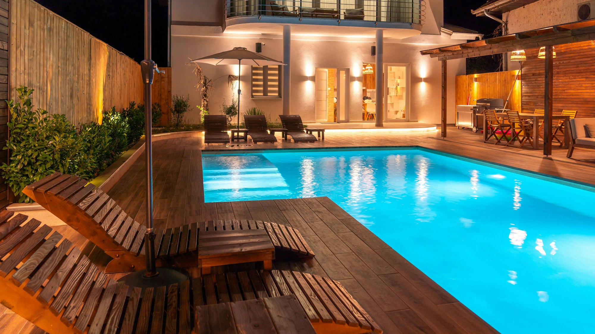 Luxusvilla mit beleuchtetem Schwimmbad und Holzliegen bei Nacht