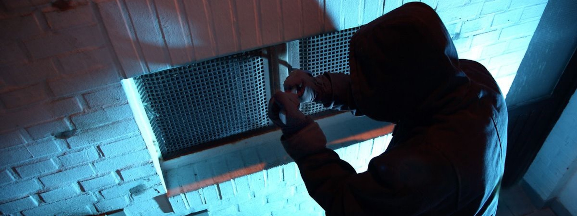 Ein Einbrecher steigt durch ein Kellerfenster ein.