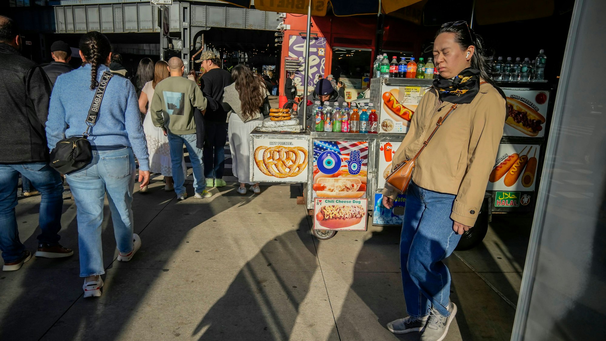Belebte Straße mit Hotdog-Stand und Passanten unter einer Brücke