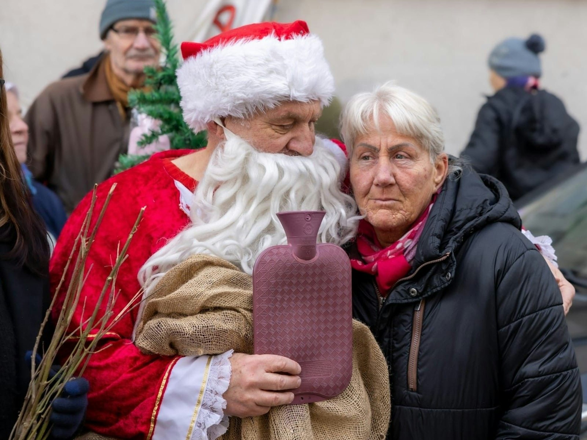 Ein als Weihnachtsmann verkleideter Mann hält Monika Steckel im Arm, in der anderen Hand hält er eine Wärmflasche.