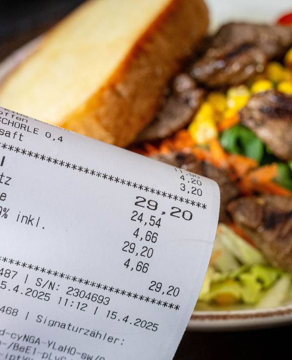 Eine Rechnung mit Mehrwertsteuer neben einem vollen Teller in einem Restaurant. Für die Gastronomie gibt es gute Nachrichten ausd em Bundesrat.