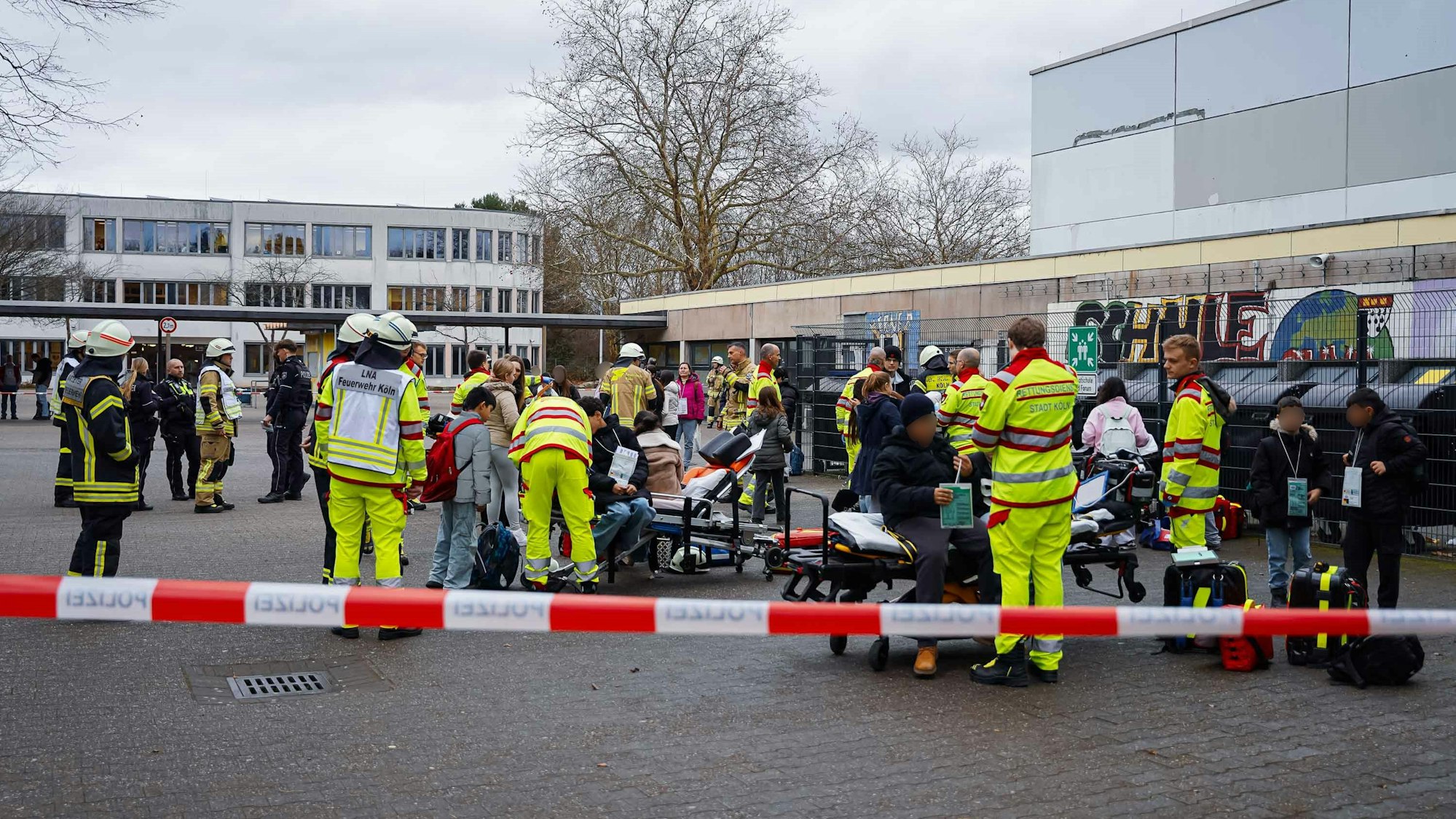 Kräfte von Feuerwehr und Rettungsdienst kümmern sich auf einem Schulhof um Schülerinnen und Schüler.