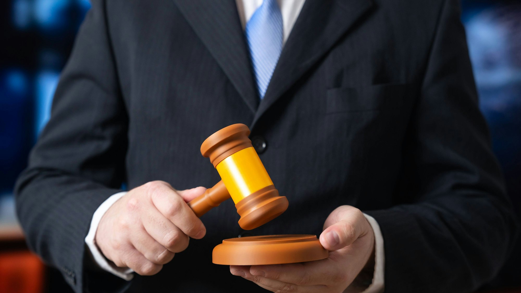 Mann im Anzug hält Richterhammer und Schlagplatte