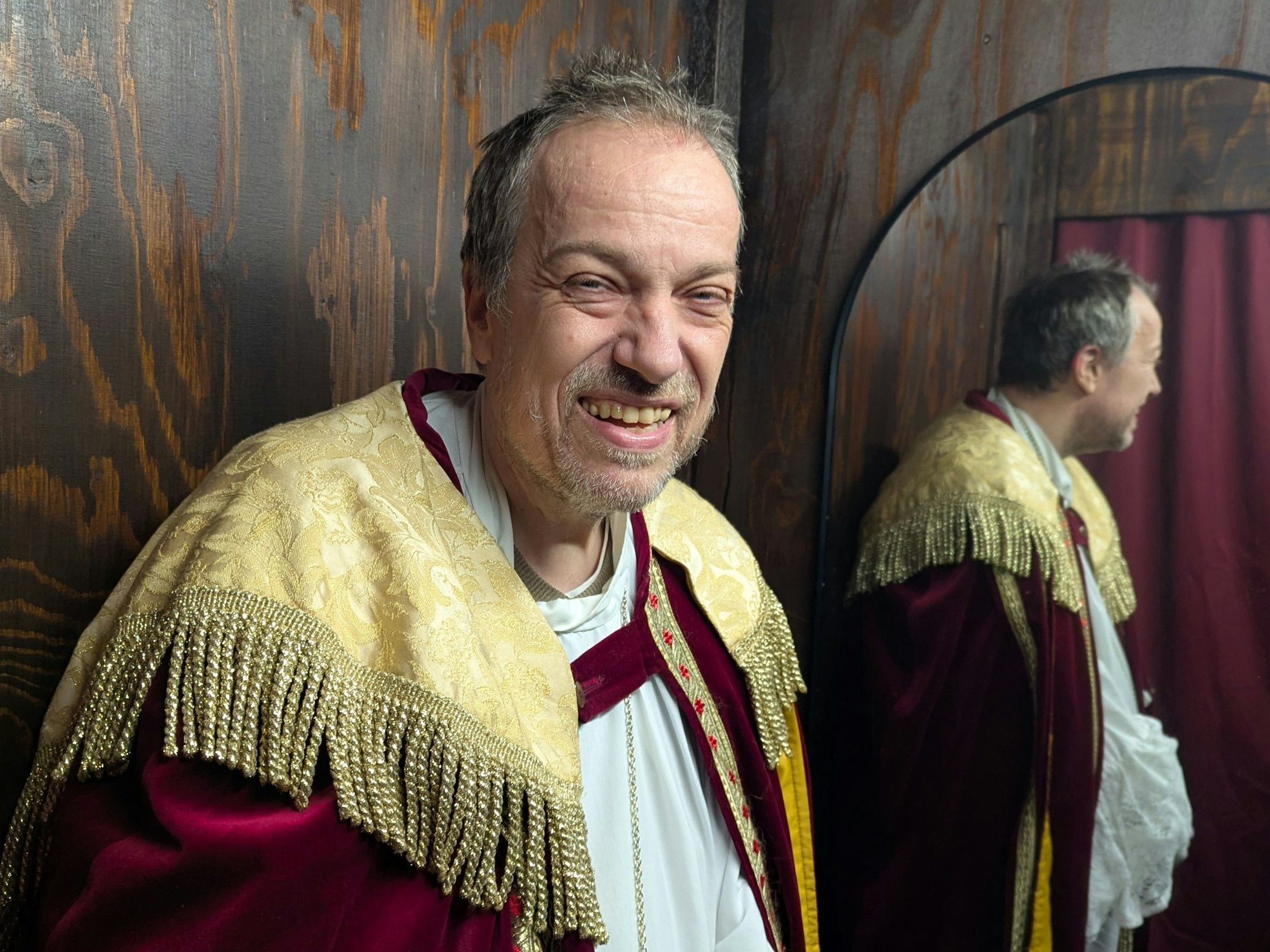 Ein Mann in der Verkleidung von Bischof Nikolaus steht vor einem Spiegel und lacht erleichtert