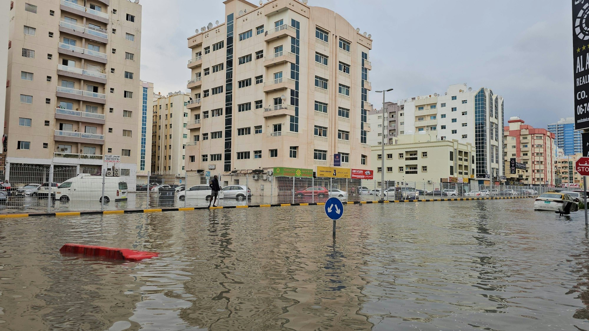 Überflutete Straße mit Gebäuden, Fahrzeugen und Person
