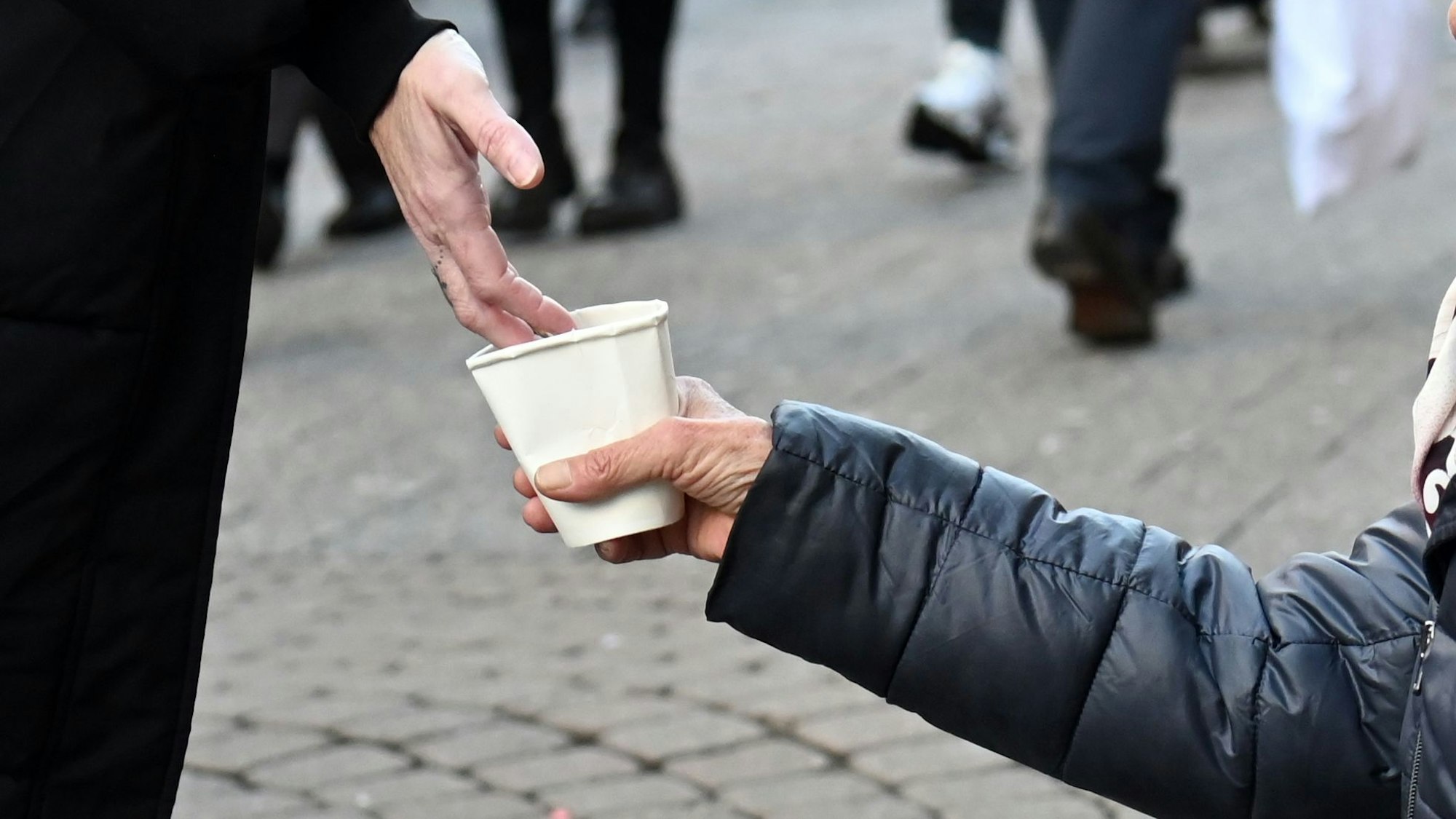 Ein Mann wirft in der Kölner Innenstadt Geld in einen Becher einer Bettlerin.