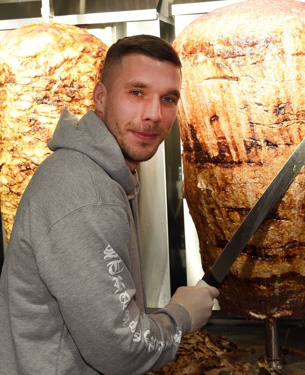 Fußball-Weltmeister Lukas Podolski steht am 6. Januar 2018 in Köln bei der Eröffnung eines Döner-Ladens an einem Dönerspieß.