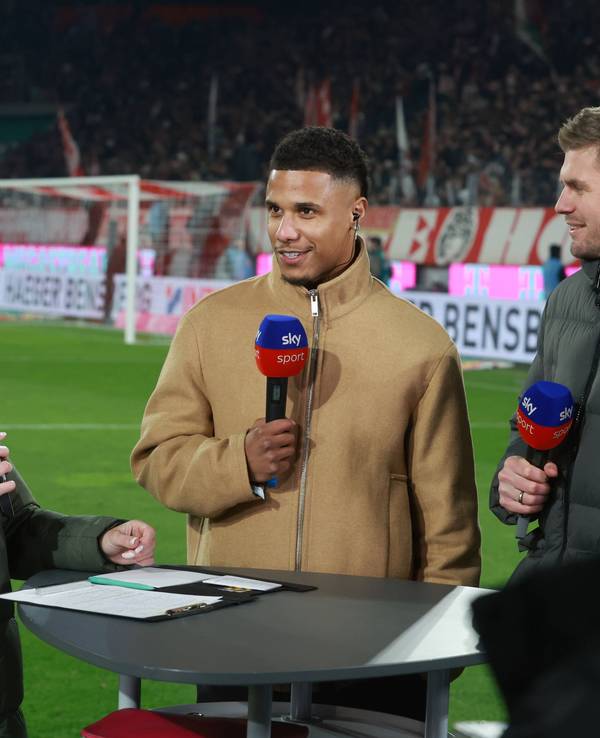 Ismail Jakobs steht bei Sky am Tisch und spricht in ein Mikrofon.
