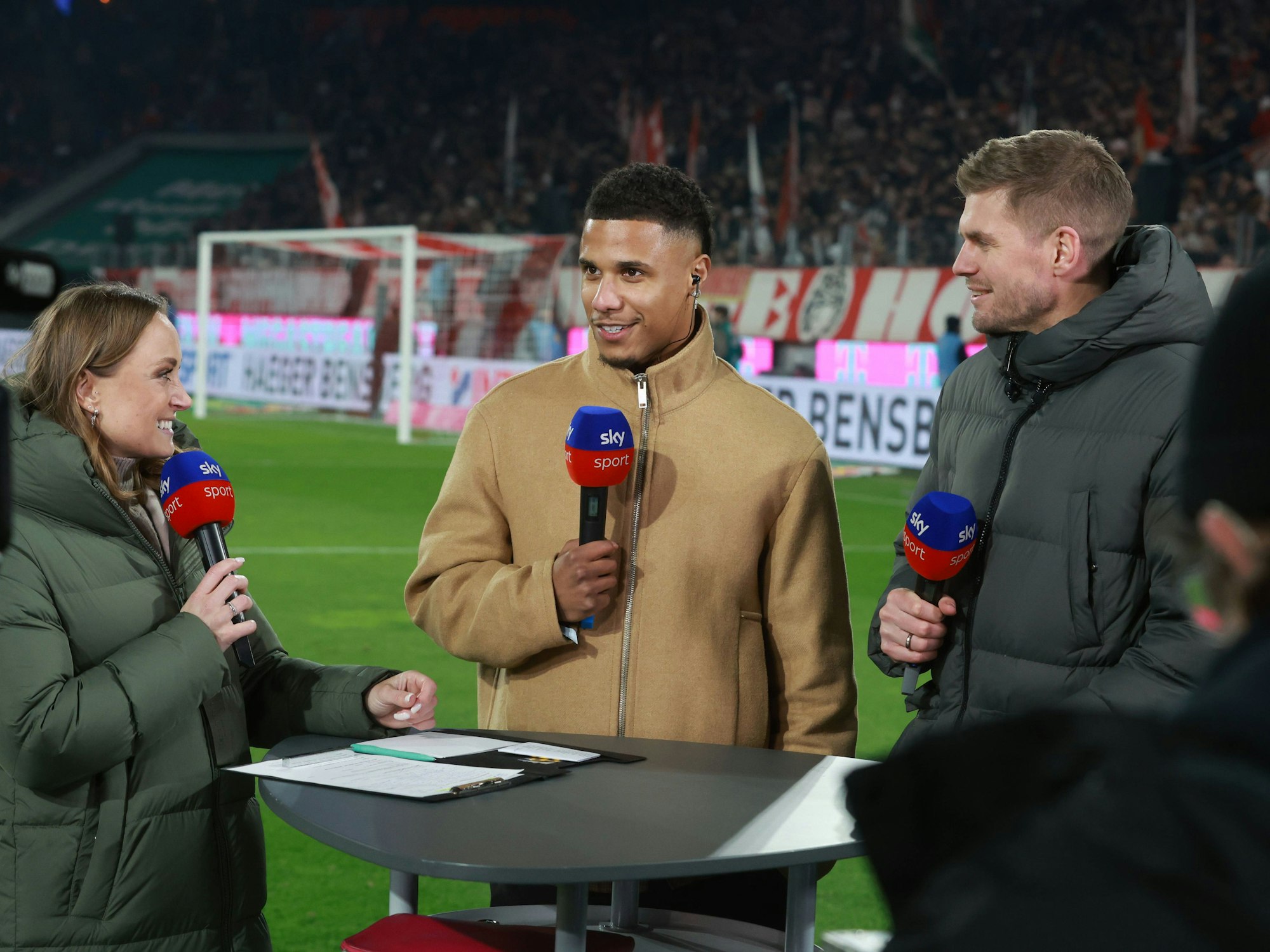 Ismail Jakobs steht bei Sky am Tisch und spricht in ein Mikrofon.