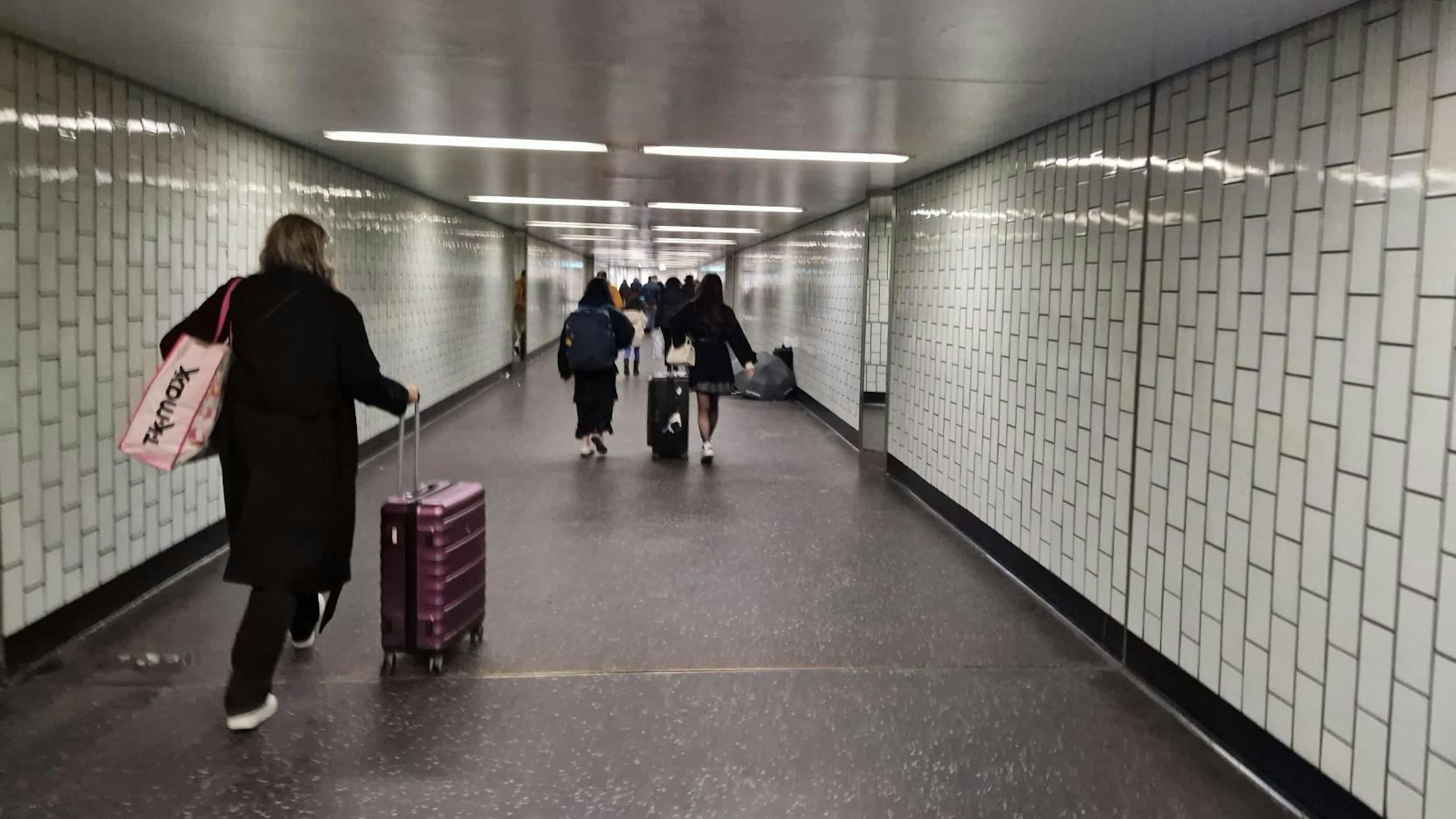 Menschen mit Koffern gehen durch eine Unterführung.