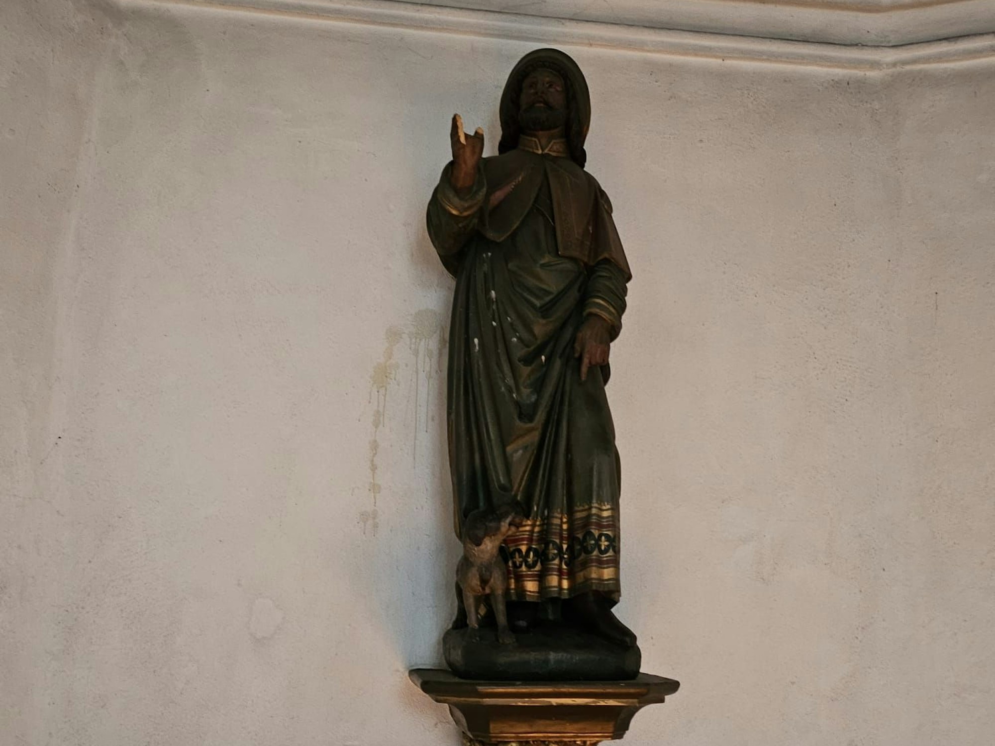 Die Figur eines Heiligen steht auf einem Sockel an einer Wand.
