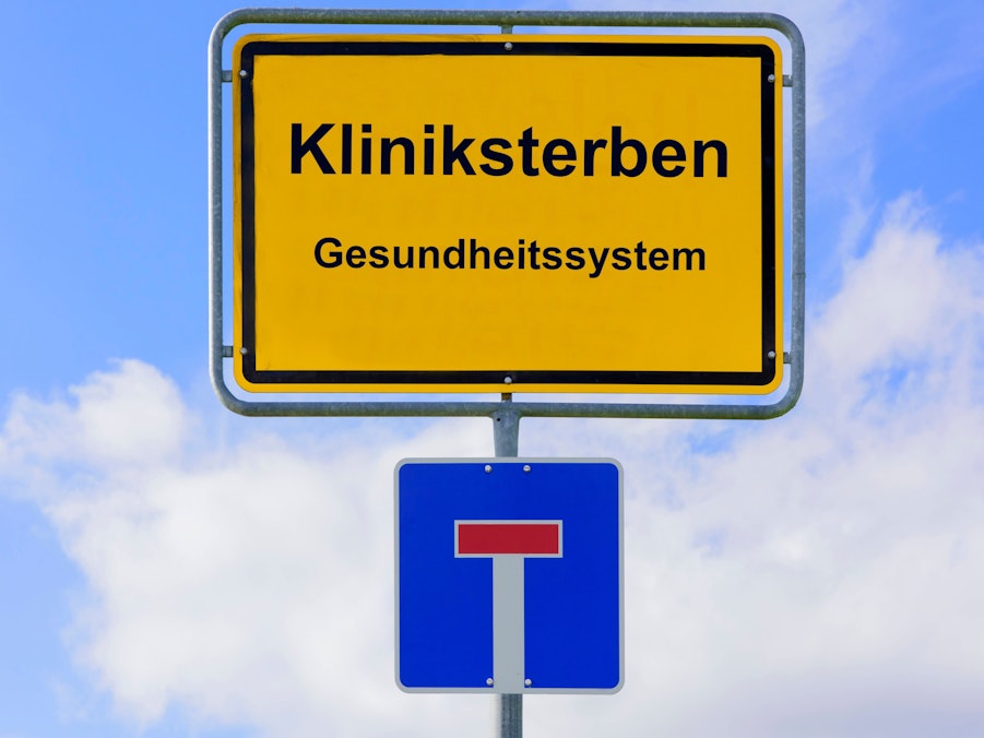 Schilder mit „Kliniksterben“, „Gesundheitssystem“ und Sackgassensymbol