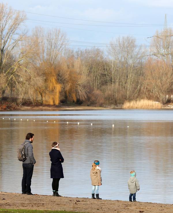 Zwei Erwachsene und zwei Kinder stehen an einem Wintertag am Ufer eines Sees und blicken übers Wasser.