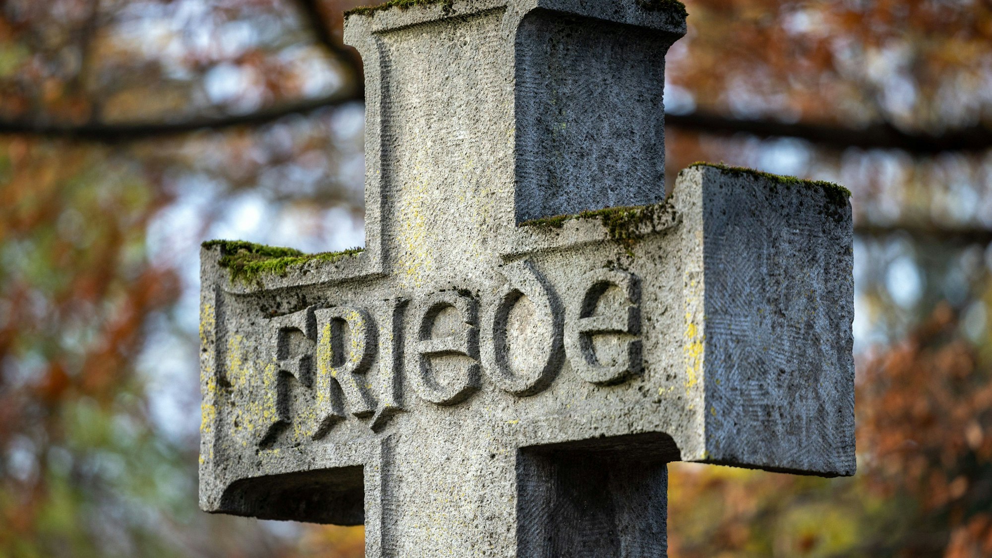 Steinernes Kreuz mit Inschrift „Friede“ auf Friedhof