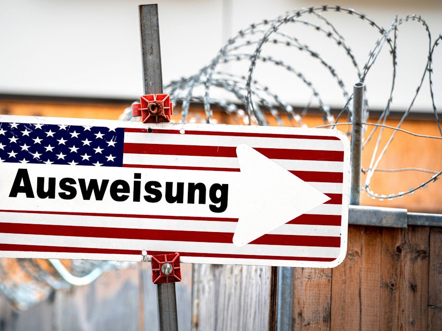 Schild mit US-Flagge und Aufschrift „Ausweisung“ vor Stacheldraht