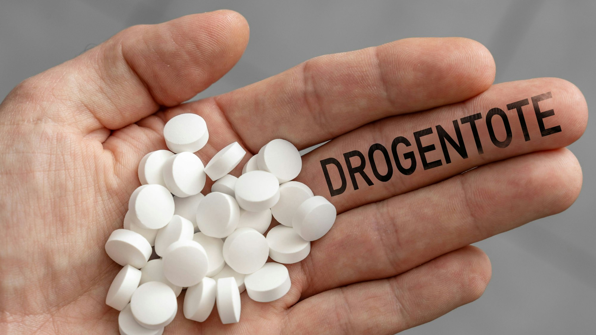 Eine Hand hält Tabletten und den Schriftzug „Drogentote“