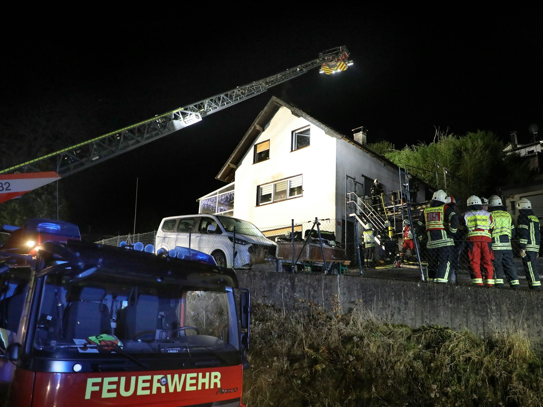 Eine Feuerwehrdrehleiter steht vor einem Haus, das offenbar gebrannt hat. Feuerwehrleute stehen davor.