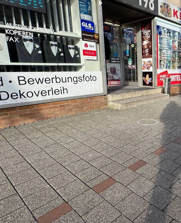 Vor einem Kiosk sind Markierungen der Spurensicherung auf dem Bürgersteig. Ein 27-jähriger Mann ist in Dortmund auf offener Straße von mehreren Kugeln getroffen worden.