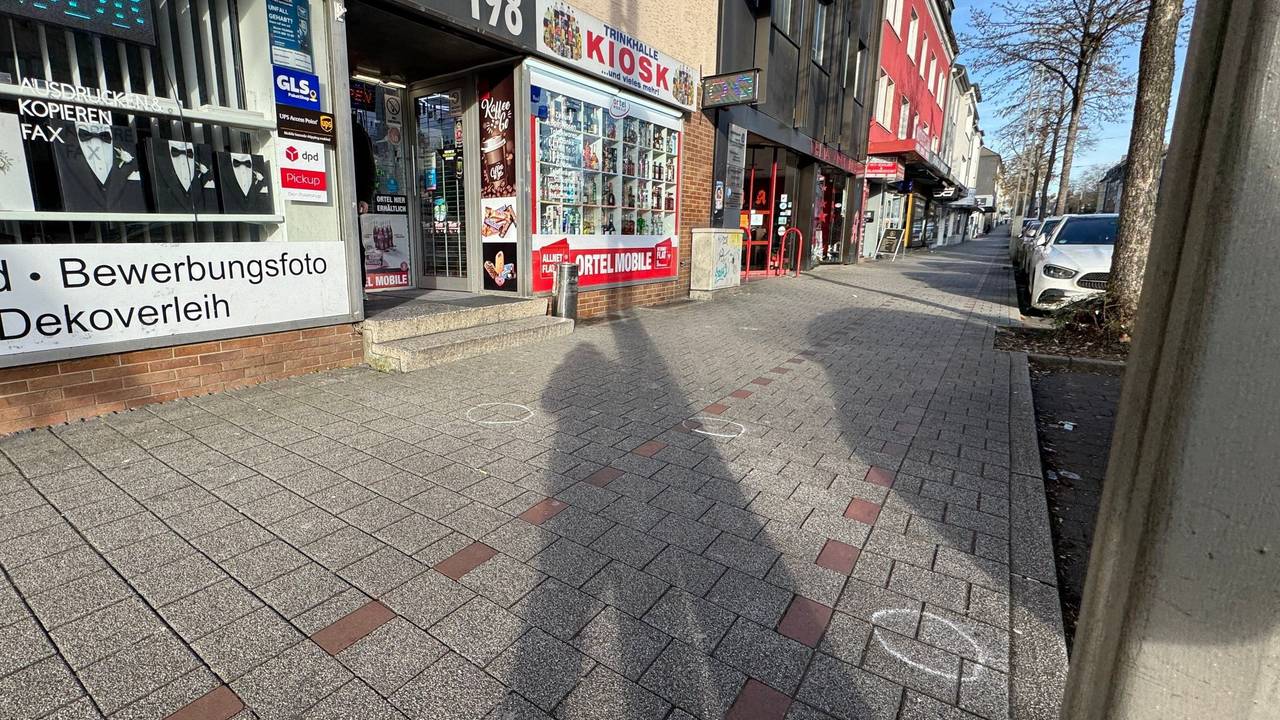 Vor einem Kiosk sind Markierungen der Spurensicherung auf dem Bürgersteig. Ein 27-jähriger Mann ist in Dortmund auf offener Straße von mehreren Kugeln getroffen worden.