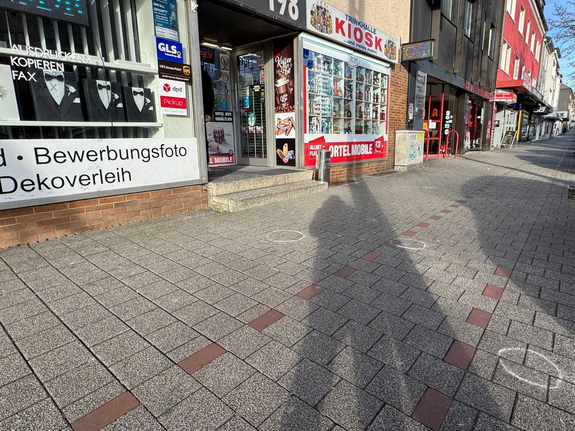 Vor einem Kiosk sind Markierungen der Spurensicherung auf dem Bürgersteig. Ein 27-jähriger Mann ist in Dortmund auf offener Straße von mehreren Kugeln getroffen worden.