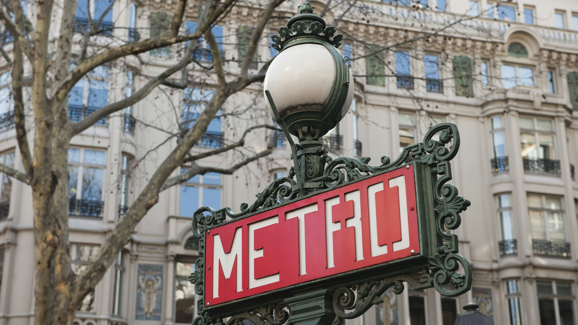 Verziertes Schild an Laterne vor Gebäude mit Baum