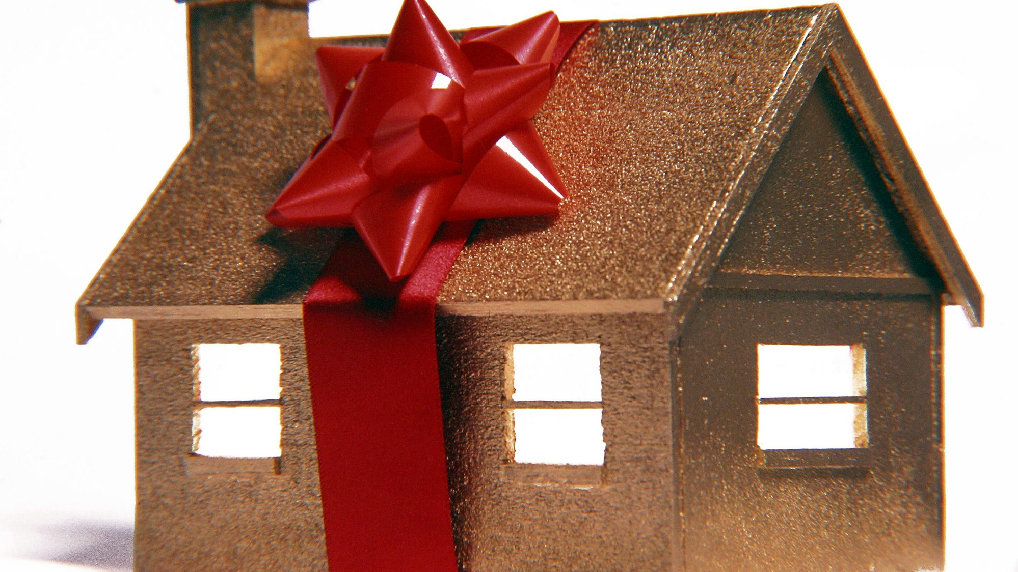 Golden glänzendes Modell-Haus ist mit rotem Geschenkband umwickelt