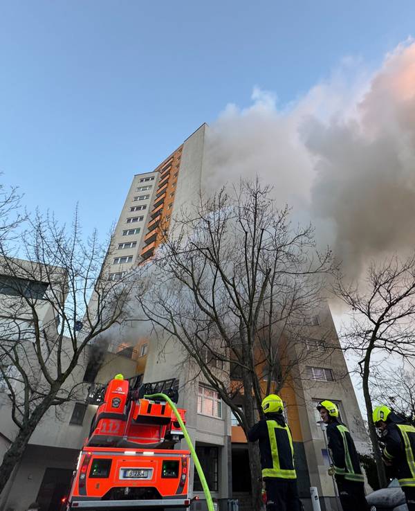 Einsatzfahrzeuge von Rettungskräften und Feuerwehr stehen vor einem Hochhaus, aus dem Rauch aufsteigt. In Berlin-Spandau brennt seit den frühen Morgenstunden ein Hochhaus.