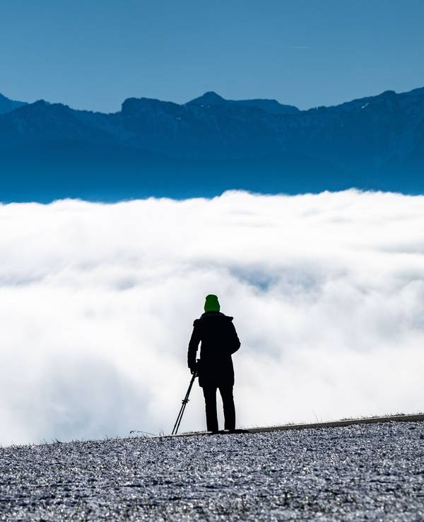 Eine Person blickt über eine Wolkendecke auf ein Bergpanorama.