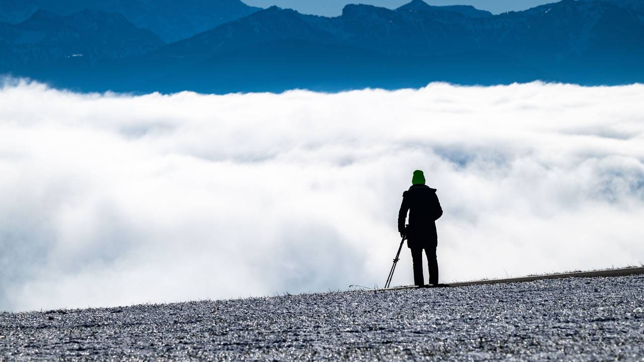 Eine Person blickt über eine Wolkendecke auf ein Bergpanorama.