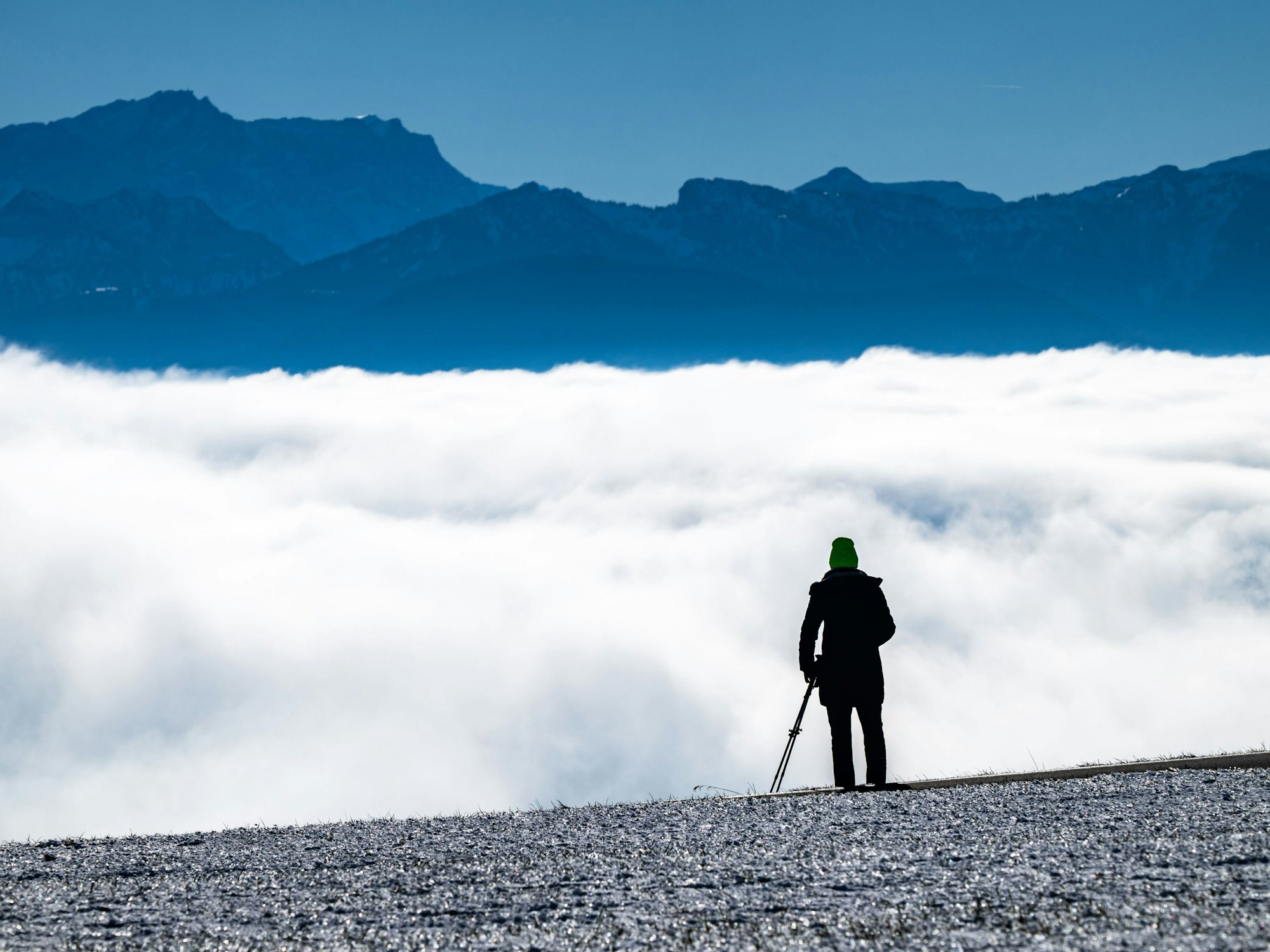 Eine Person blickt über eine Wolkendecke auf ein Bergpanorama.