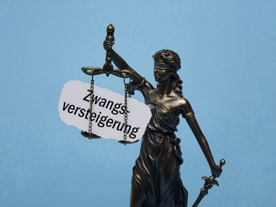 Justitia mit Waage und dem Schriftzug „Zwangsversteigerung“