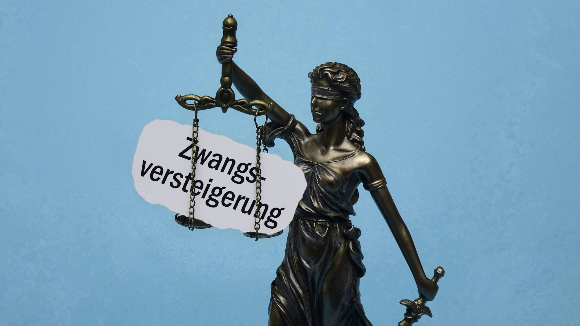 Justitia mit Waage und dem Schriftzug „Zwangsversteigerung“