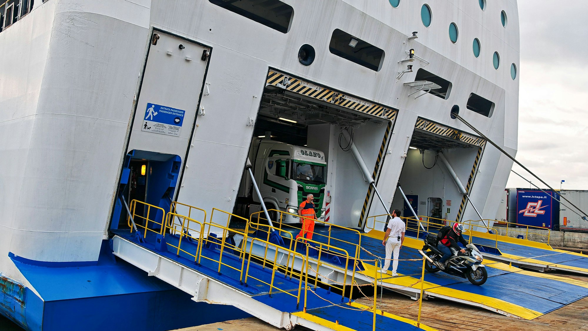 LKW, Motorrad und Menschen verlassen eine Fähre