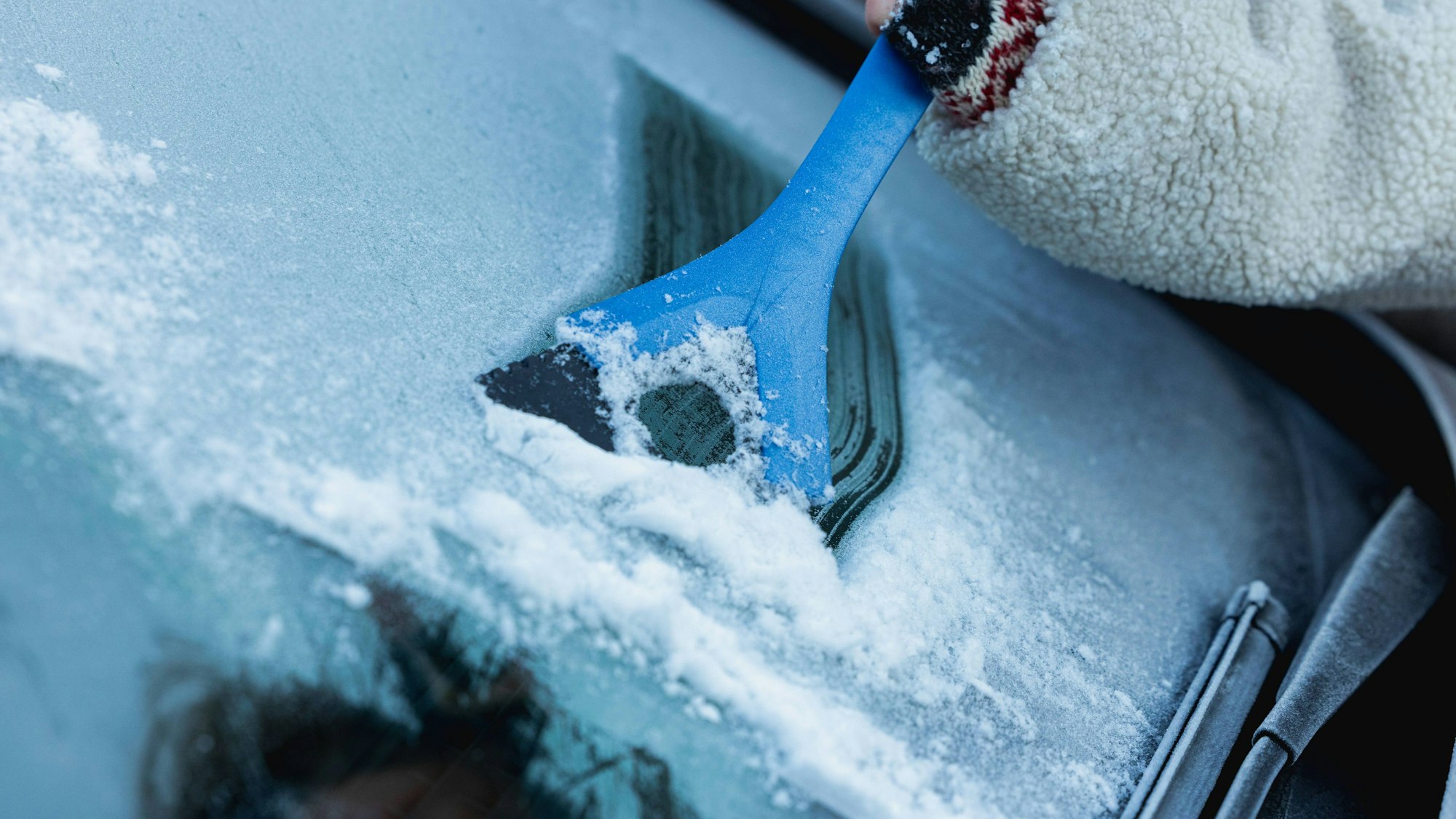 Person befreit Autoscheibe von Eis und Schnee