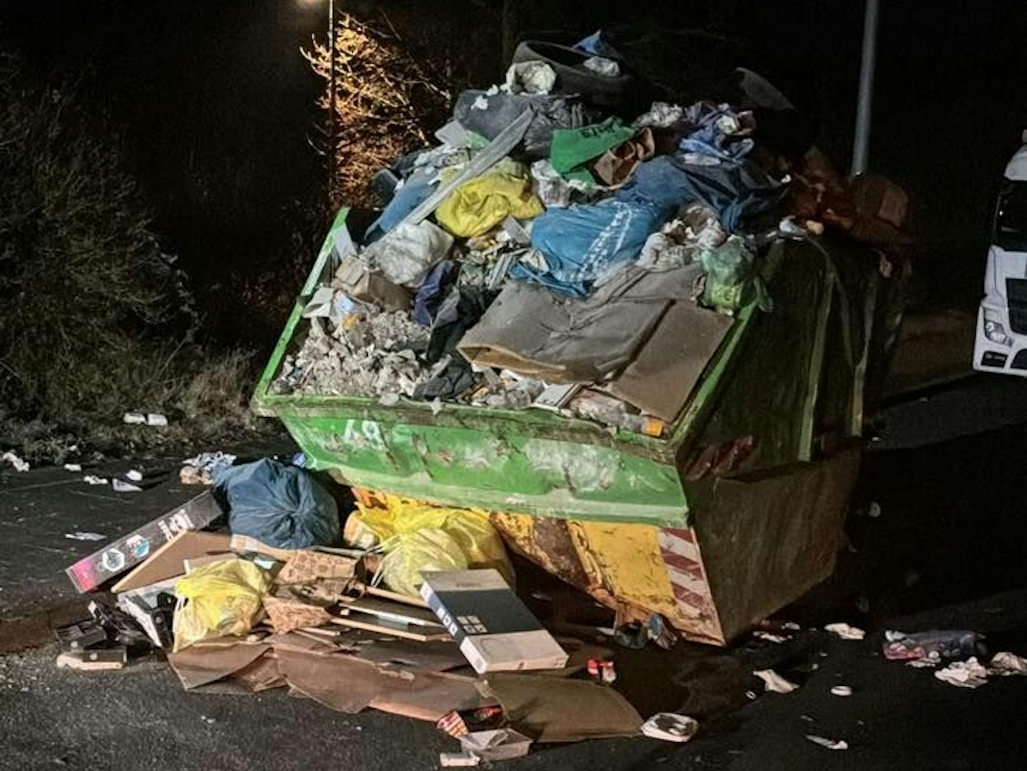 Ein Müllcontainer ist übervoll, auch auf dem Boden um ihn herum liegt Müll.