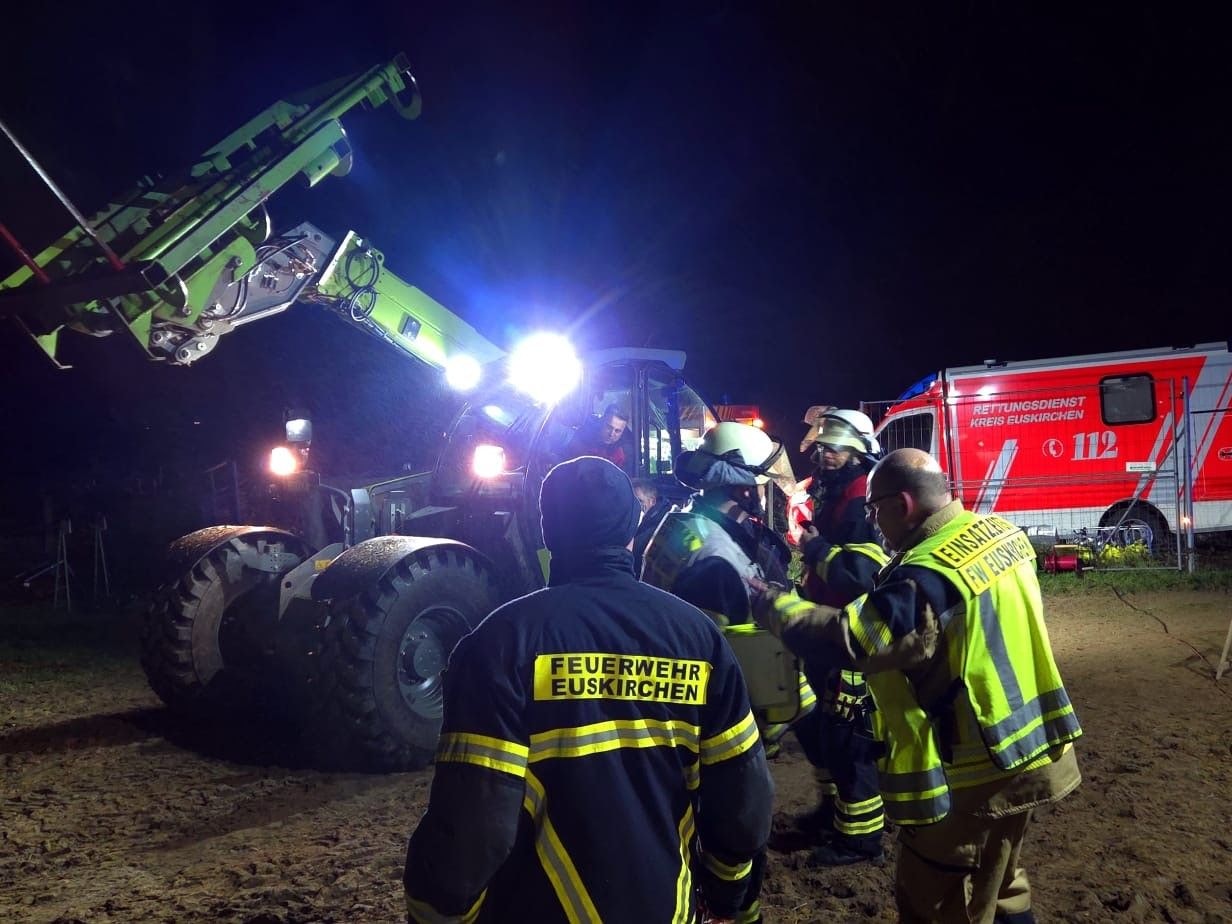 Einsatzkräfte der Feuerwehr stehen vor einem Radlader.