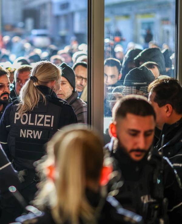 Menschen stehen vor dem Eingang zur Sparkasse, den Polizeikräfte versperren.